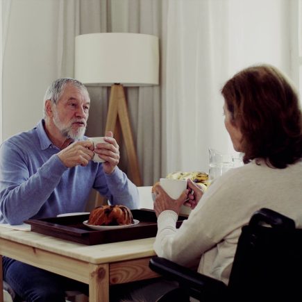 Retired couple at different life stages, with one partner dressed for work and the other relaxing at home, highlighting the tension and transition of mismatched retirement timing