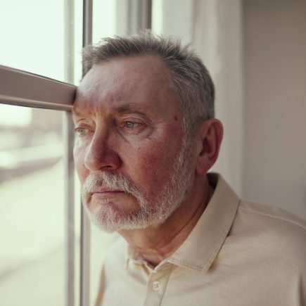 Retired person sitting near a window, looking reflective and quiet, symbolizing emotional transition and the sense of loss that can come with retirement
