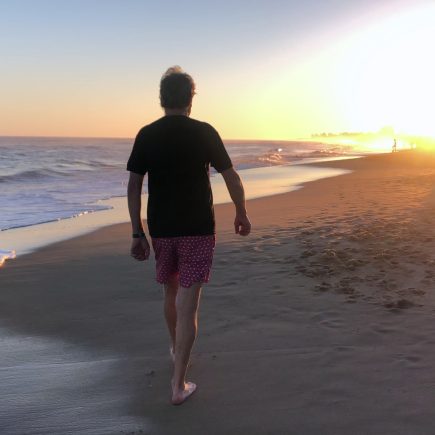 Retired man walking alone on beach, reflecting on how quickly summer is passing by